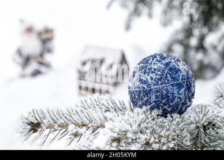 Primo piano di ornamento di natale su albero di copertura con neve e Babbo Natale a piedi cottage in background Foto Stock