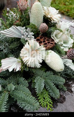 Scatto verticale di una disposizione floreale con fiori e rametti di abete su una tomba Foto Stock