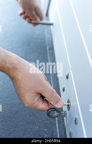 Primo piano di una mano con una chiave che chiude lo sportello dell'otturatore a rullo di un negozio. Concetto di chiusura Foto Stock
