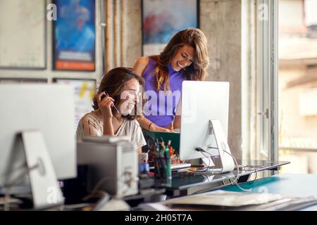 due giovani colleghi caucasici ridono al lavoro, sorridono, lavorano insieme, si divertono al lavoro Foto Stock