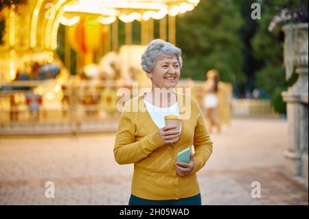 Granny con una tazza di caffè al telefono nel parco Foto Stock