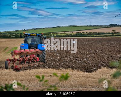 Un trattore agricolo che aratura un campo di stoppie in una giornata parzialmente soleggiata in autunno. Preso in Northumberland, Inghilterra, Regno Unito. Foto Stock