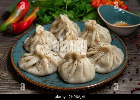 Khinkali in stile georgiano con carne su un piatto di ceramica fatto a mano. Cospargere con pepe macinato. Foglie di prezzemolo e coriandolo sullo sfondo. Su a d Foto Stock