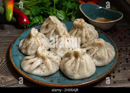 Khinkali in stile georgiano con carne su un piatto di ceramica fatto a mano. Cospargere con pepe macinato. Foglie di prezzemolo e coriandolo sullo sfondo. Su a d Foto Stock