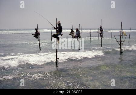 SRI LANKA: I pescatori di Tangalle sospesi sul mare nel modo in cui fanno la loro tecnica tradizionale per catturare il pesce su pali Foto Stock