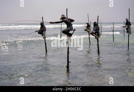 SRI LANKA: I pescatori di Tangalle sospesi sul mare nel modo in cui fanno la loro tecnica tradizionale per catturare il pesce su pali Foto Stock