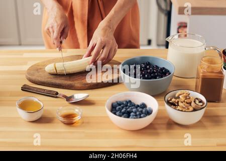 Mani di giovane femmina tritare banana su tavola di legno per frullati fatti in casa Foto Stock