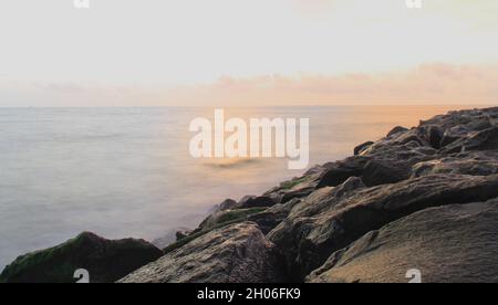 La lunga esposizione è stata scattata dalla spiaggia durante il tramonto con le rocce in primo piano Foto Stock