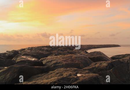 Foto a lunga esposizione scattata dalla spiaggia al tramonto con rocce in primo piano Foto Stock