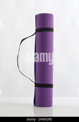 Tappeto di yoga viola arrotolato isolato su sfondo bianco Foto Stock