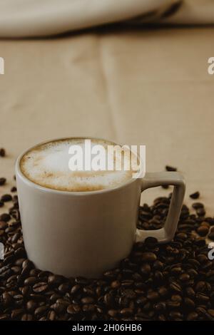 Tazza di caffè latte sul fondo dei chicchi di caffè su sfondo marrone. Fotografia del caffè di Still Life. Foto Stock