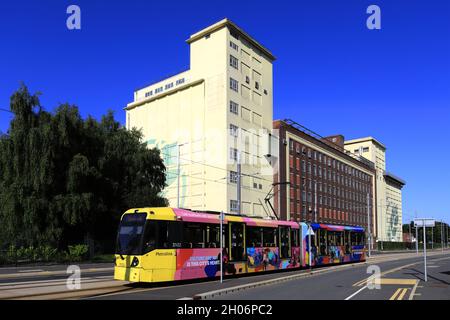 Tram che passa per il mulino Whitworth Brothers, Trafford Wharf Rd, Manchester, Lancashire, Inghilterra, REGNO UNITO Foto Stock