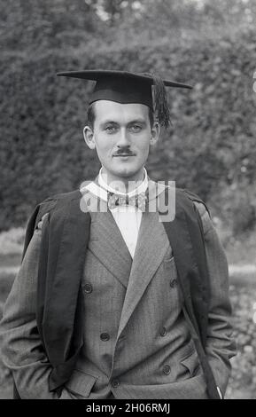 Anni '50, storico, un giovane inglese con un baffo corto e indossando un abito a doppia prora e una cravatta ad arco in posa per la sua foto in un abito da laurea e cappellino accademico quadrato, spesso definito come cappellino e abito, Inghilterra, Regno Unito. Indossato con regalia accademica alle cerimonie di laurea, il suo tipo speciale di cappellino è noto come un mortarboard o a volte come cappellino Oxford e consiste di una tavola quadrata orizzontale fissata su un cappellino cranio con un tasello attaccato al centro. Il suo aspetto distintivo significa che la PAC è associata al mondo accademico. Foto Stock