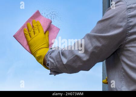 Uomo contemporaneo lavando finestre a casa, panni rosa, guanti di gomma gialli, concetto di pulizia della casa, eseguito anche da uomini Foto Stock