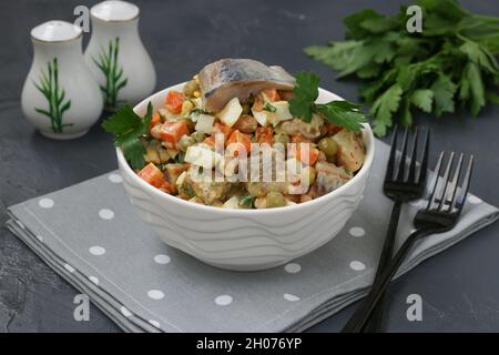 Insalata di aringhe con carote, uova e piselli in un recipiente bianco su sfondo scuro Foto Stock