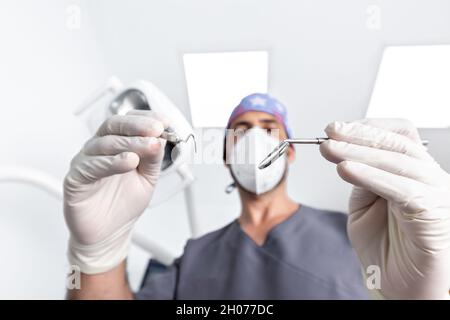 Fuoco selettivo sugli attrezzi che stanno usando un dentista maschio con uniforme e maschera in una clinica dentale Foto Stock