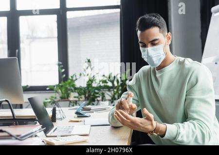 Uomo d'affari musulmano in maschera medica spray igienizzatore a mano in ufficio Foto Stock