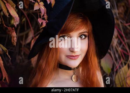 Halloween Witch redhead donna facendo stregoneria con magic Libro di incantesimi, magia nelle sue mani. Bella giovane donna in streghe cappello conjuring. Spooky Foto Stock