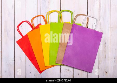 Un arcobaleno di sacchetti di carta colorati su un elegante tavolo di legno per il vostro shopping gioioso. Spazio per il logo o una scritta sulla borsa viola. Foto Stock