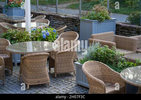 Terrazza estiva in hotel o ristorante con intimi mobili in vimini di legno, piante verdi e nessuna gente Foto Stock