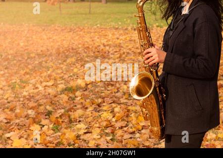 Una donna suona il sassofono in un parco autunnale. Primo piano del sassofono d'oro. Spazio di copia per il testo. Foto Stock