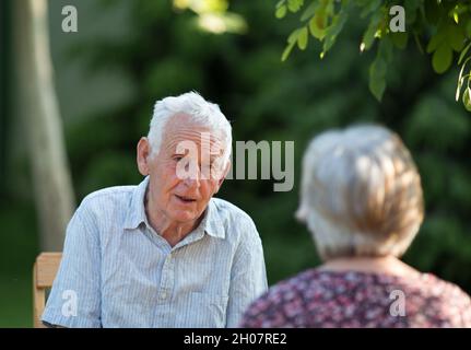 Coppia anziana seduta in giardino e parlare in estate Foto Stock