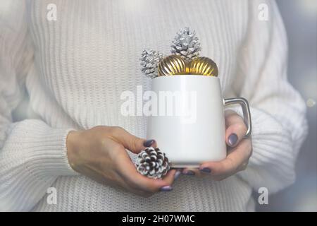 coppa di natale bianca sulle mani della donna con coni di pino-tazza di inverno primo piano per il concetto di nuovo anno Foto Stock