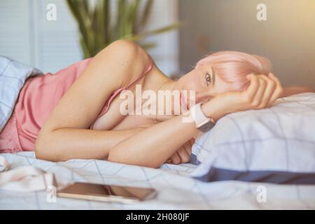 La donna graziosa si sveglia in un letto confortevole e moderno nella camera d'albergo Foto Stock