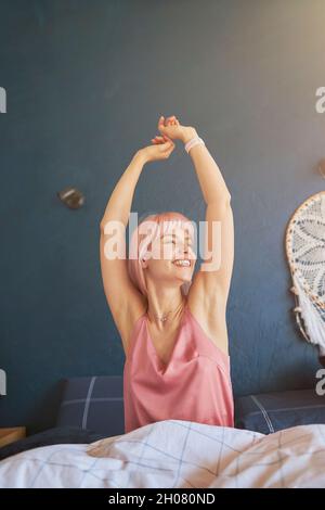 Donna gioiosa in elegante pigiama tende a svegliarsi in grande letto al mattino pigro Foto Stock