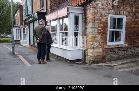 Coppia anziana che guarda attraverso una vetrina di agenti immobiliari a Thirsk, Yorkshire, Inghilterra. Foto Stock