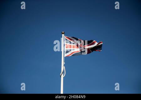 Bandiera dell'Unione del Regno Unito che vola da un flagpole bianco contro un cielo blu chiaro Foto Stock