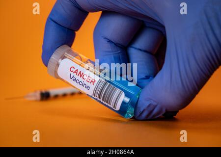 Vaccino antitumorale gloved Hand Holding con siringa su sfondo arancione Foto Stock