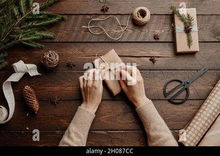 Vista dall'alto sfondo natalizio con una giovane donna irriconoscibile che avvolge regali a tavola di legno, spazio copia Foto Stock
