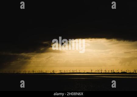 Norderney, Germania. 11 ottobre 2021. Un parco del vento è visto alla costa settentrionale dei Frisini orientali di fronte a Norderney contro il sole che aumenta creando un cielo drammatico. Credit: Matthias Oesterle/Alamy Live News Foto Stock