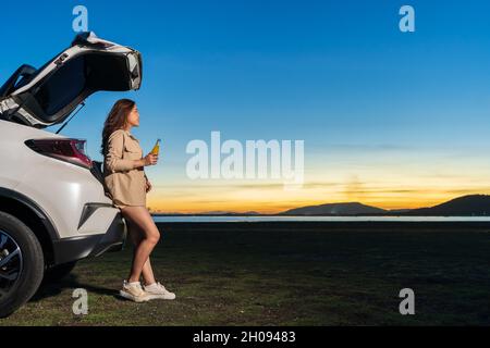 giovane donna in piedi vicino ad una macchina godendo in campo al tramonto Foto Stock