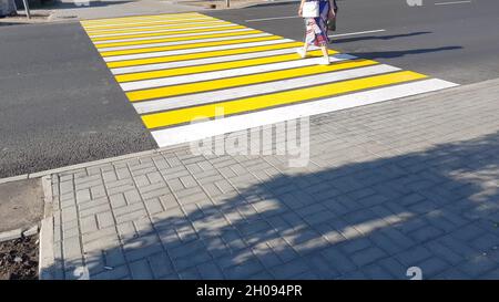 due pedoni che attraversano la strada su una nuova marcatura giallo-bianca di un passaggio pedonale, sicurezza della vita, concetto di trasporto. Foto Stock