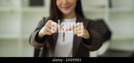 Immagine ritagliata dell'agente immobiliare femminile che mostra la catena di chiavi della casa alla telecamera. Concetto aziendale dell'albergo Foto Stock