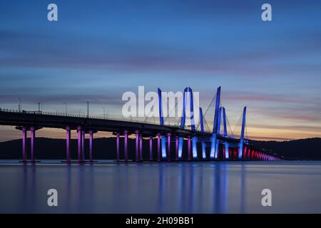 Il Governatore Mario M. Cuomo Bridge, illuminato in rosso, bianco e blu in riconoscimento del Columbus Day, attraversa il fiume Hudson subito dopo il tramonto. Foto Stock