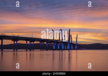 Il Governatore Mario M. Cuomo Bridge, illuminato in rosso, bianco e blu in riconoscimento del Columbus Day, attraversa il fiume Hudson poco prima del tramonto. Foto Stock