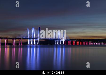 Il Governatore Mario M. Cuomo Bridge, illuminato in rosso, bianco e blu in riconoscimento del Columbus Day, attraversa il fiume Hudson subito dopo il tramonto. Foto Stock