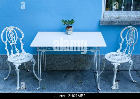 Tavolo in ferro d'epoca dipinto di bianco e sedie di fronte a una parete dipinta di blu chiaro Foto Stock