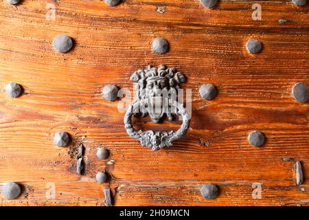 Primo piano di una massiccia porta medievale in legno con porta in ferro ornato bussare e chiodi Foto Stock