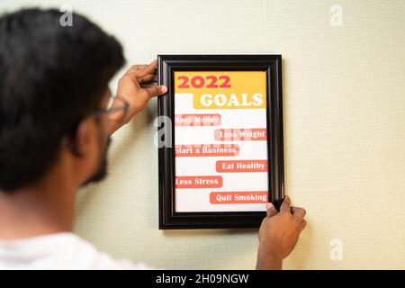 Spalla del giovane uomo che pone 2022 obiettivi sul muro - concetto di nuovo anno di impostazione degli obiettivi. Foto Stock