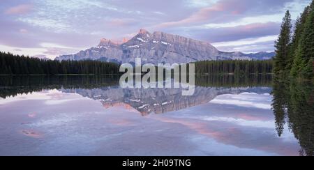 Tranquilla e colorata alba con montagna dominante che si riflette sulla superficie del lago fermo, Banff National Park, Canada Foto Stock