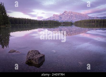 Tranquilla e colorata alba con montagna dominante che si riflette sulla superficie del lago fermo, Banff National Park, Canada Foto Stock