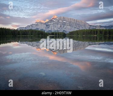 Tranquilla e colorata alba con montagna dominante che si riflette sulla superficie del lago fermo, Banff National Park, Canada Foto Stock