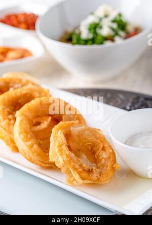 Deliziosi calamari su un piatto di porcellana bianca con insalata e salsa Foto Stock