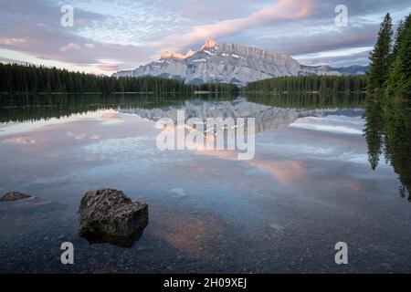 Tranquilla e colorata alba con montagna dominante che si riflette sulla superficie del lago fermo, Banff National Park, Canada Foto Stock