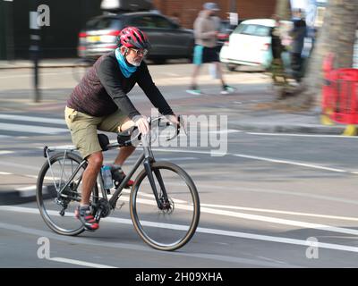 Un uomo in bicicletta su Chiswick High Road, Londra, Regno Unito Foto Stock