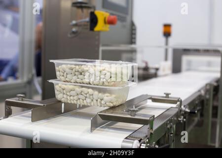 Primo piano degli alimenti in scatole di plastica sulla macchina confezionatrice dello stabilimento Foto Stock